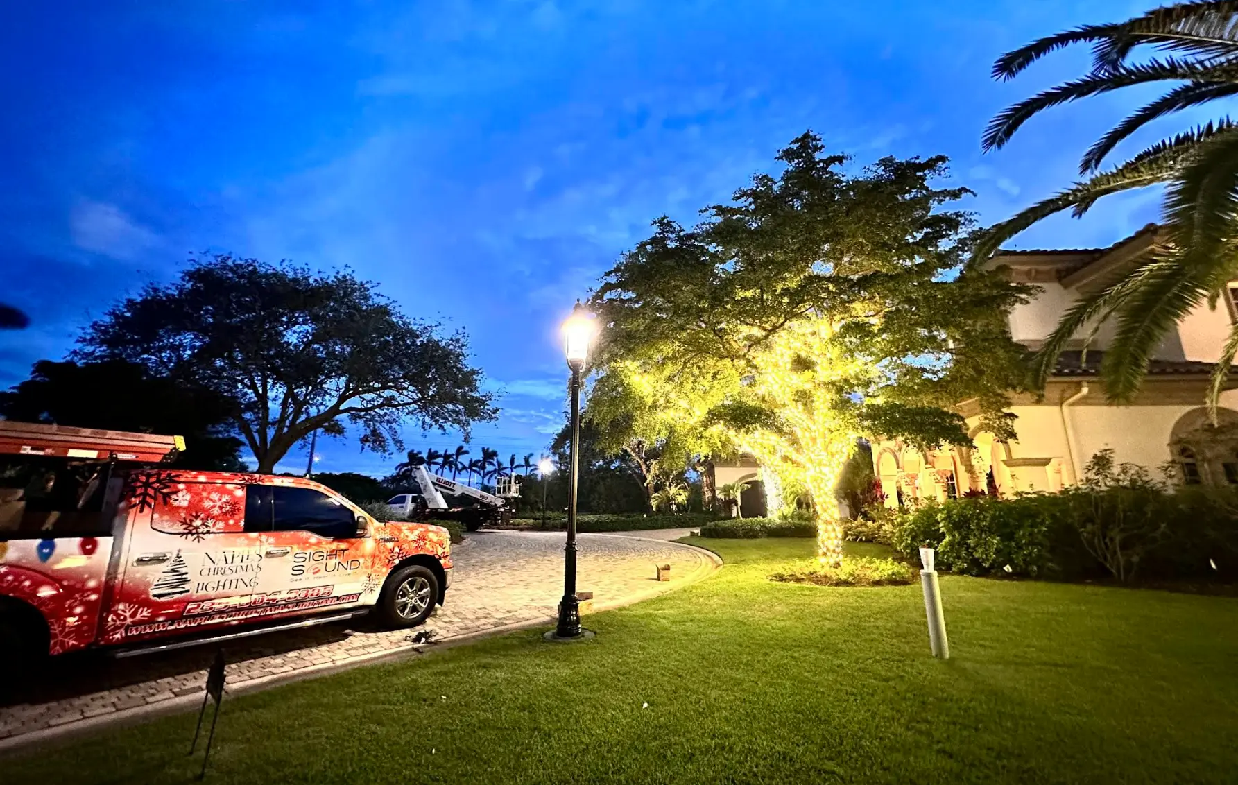 Branded Naples Christmas Lighting truck beside a lit tree at a luxury estate