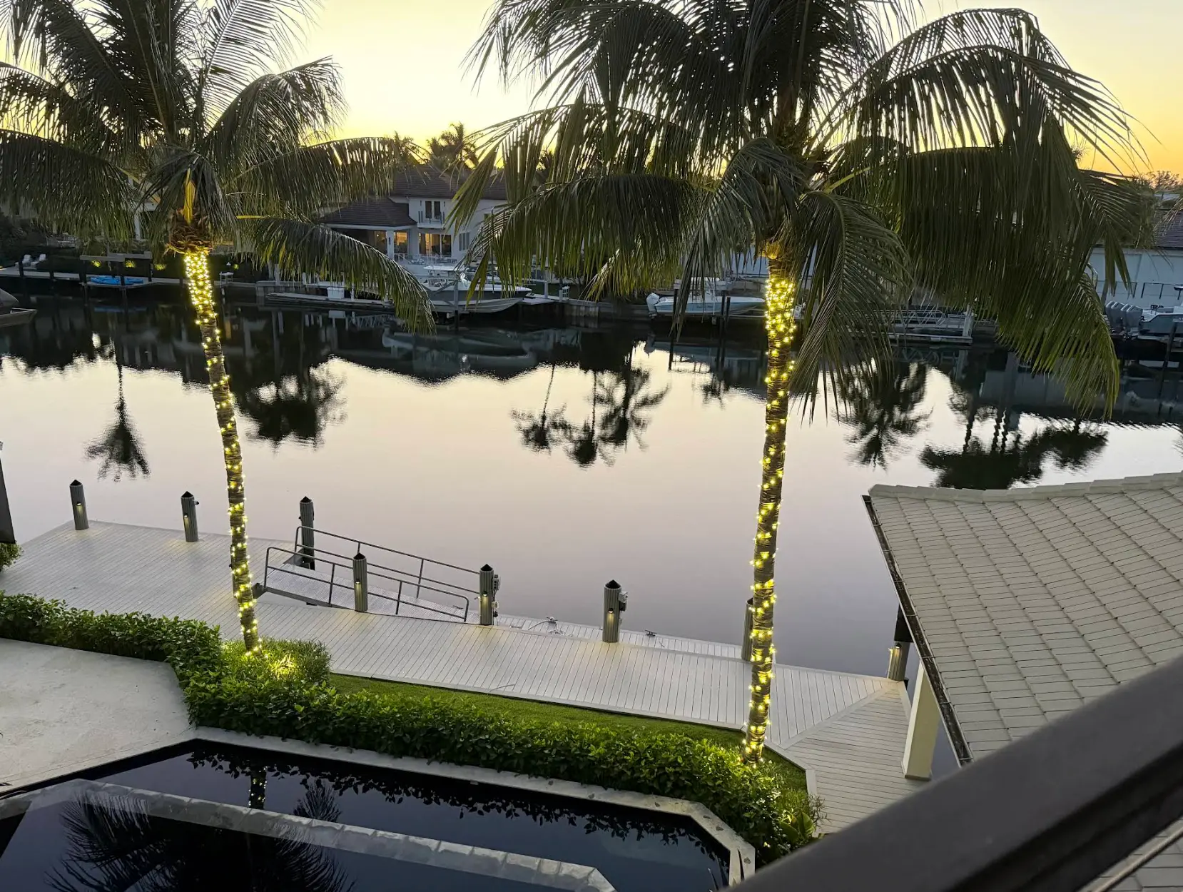 Waterfront Naples home at sunset with palms wrapped in warm white lights along a dock
