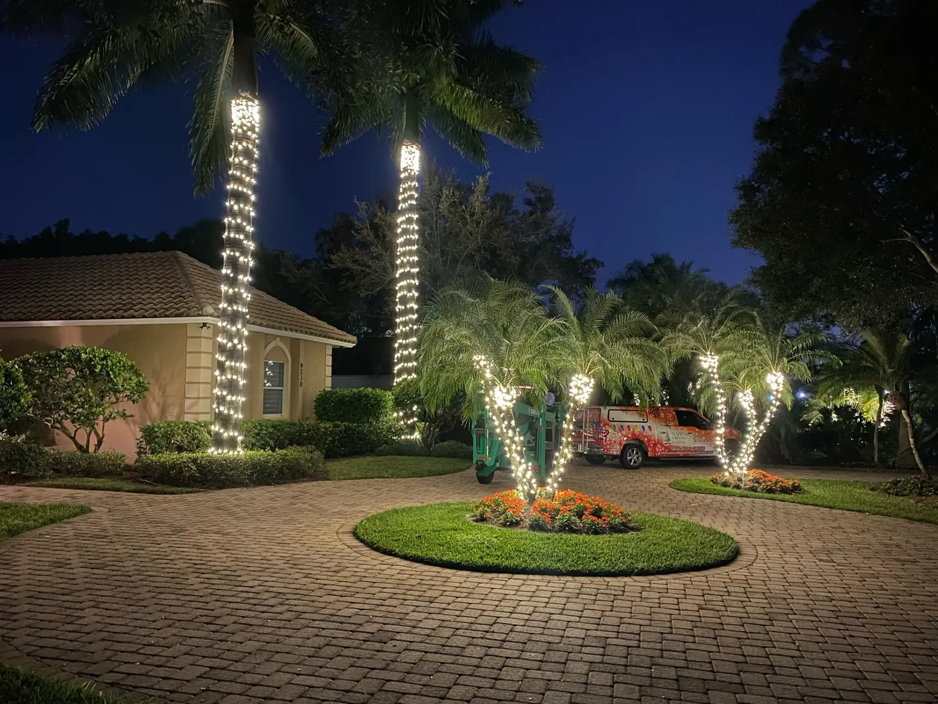 Circular paver driveway with tall palms wrapped in warm white lights
