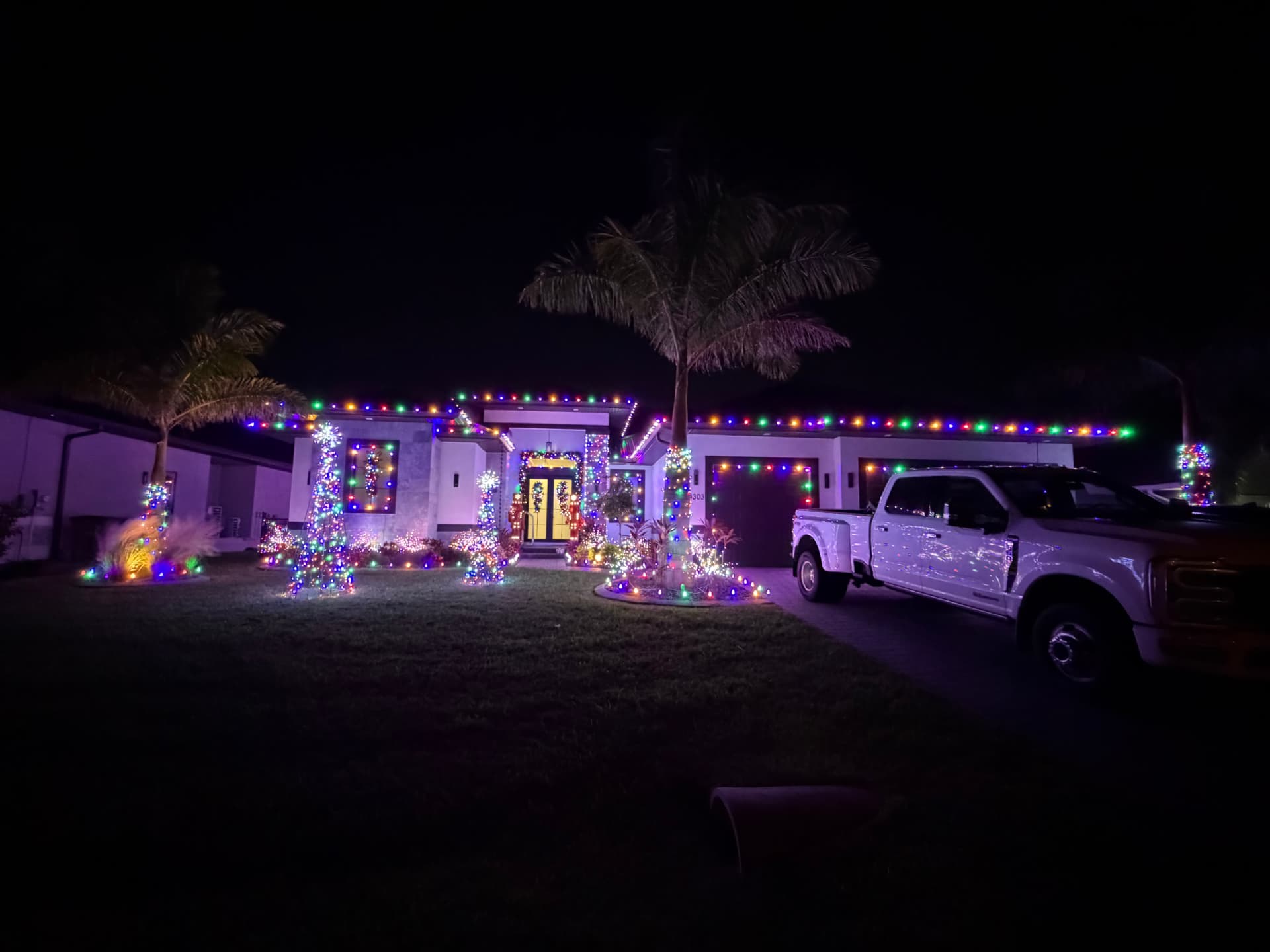 Multicolor roofline Christmas lights on a Naples home with lit palms and yard displays